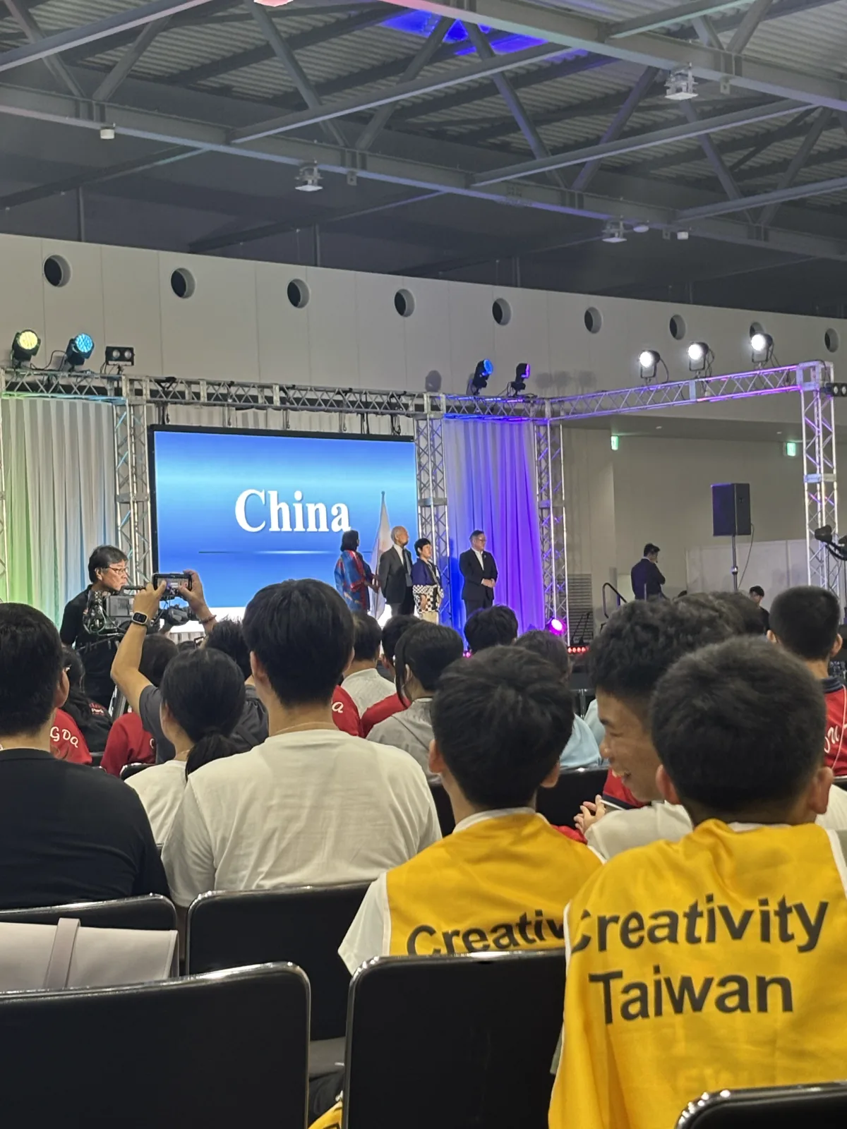穿著臺灣代表隊的隊服在會場,旁邊就是各國的攤位